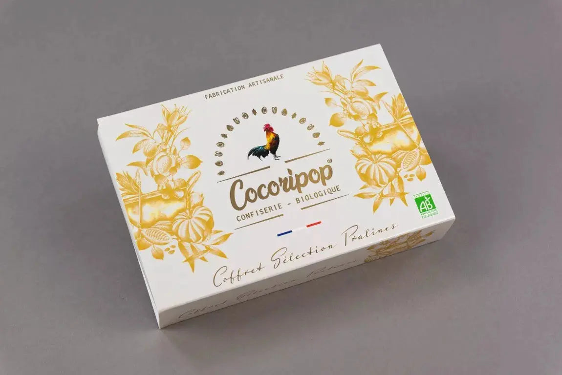 Coffret Sélection Pralines Bio – élégant coffret cadeau avec dorures contenant trois variétés de pralines artisanales : amandes, noisettes et graines de courge, présenté sur fond blanc. bio