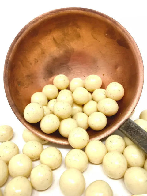 Vue rapprochée de billes de maïs croustillantes enrobées de chocolat blanc bio à la vanille, posées sur une surface en bois clair