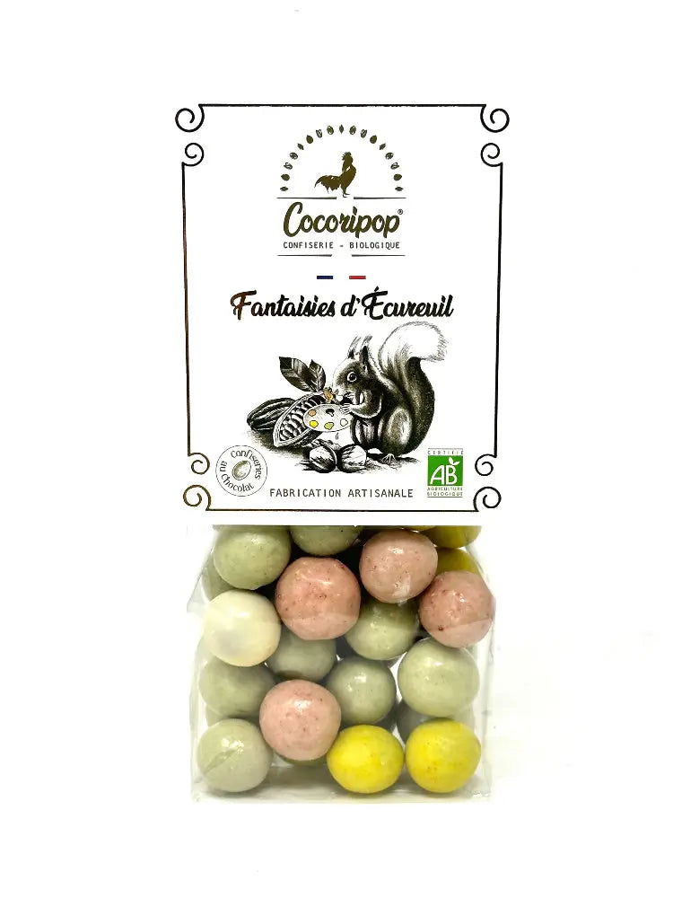 Fantaisie d'écureuil, Noisettes croquantes enrobées de chocolat au lait et blanc, déclinées en quatre couleurs gourmandes : rose, vert, blanc et jaune, présentées sur fond blanc. BIO