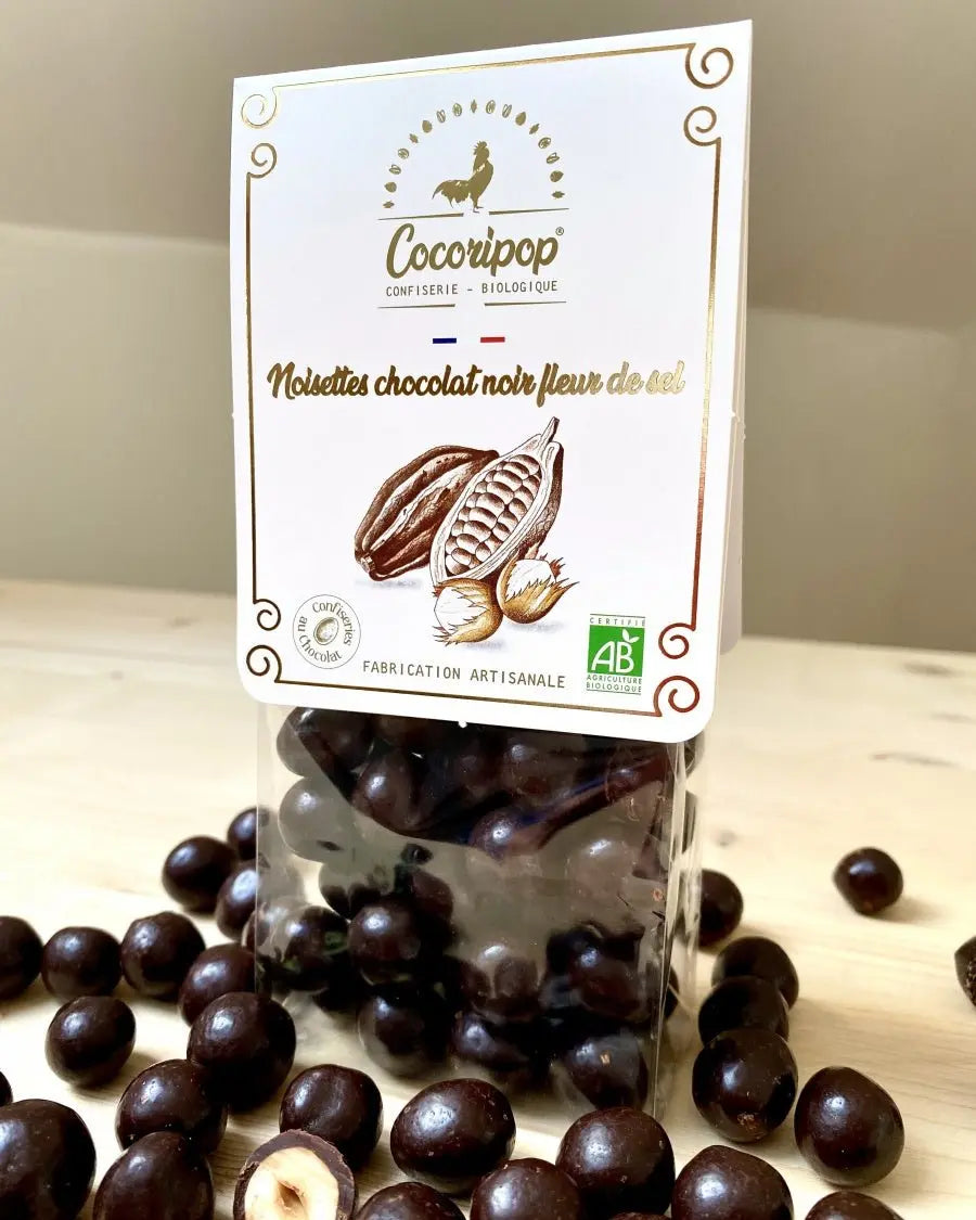 Noisettes Chocolat Noir Fleur de Sel Bio – un équilibre parfait entre le croquant des noisettes caramélisées, la puissance du chocolat noir et la délicatesse de la fleur de sel. Une mise en scène raffinée pour une expérience gustative intense. bio