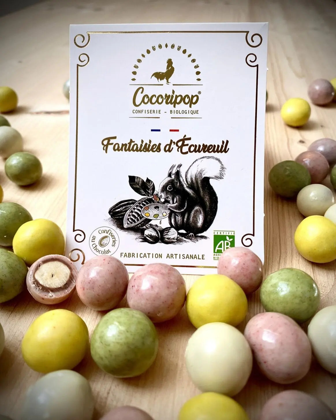 Fantaisies d'Ecureuil Bio – une explosion de saveurs et de couleurs avec des noisettes croquantes enrobées de chocolat blanc teinté naturellement à la fraise, au curcuma et à l’épinard. Une mise en scène joyeuse et gourmande. bio 